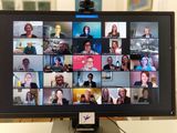 Foto eines Bildschirms, auf denen 25 Gesichter von Menschen zu sehen sind, die sich in einer Videokonferenz befinden. Viele heben Sektgläser hoch.