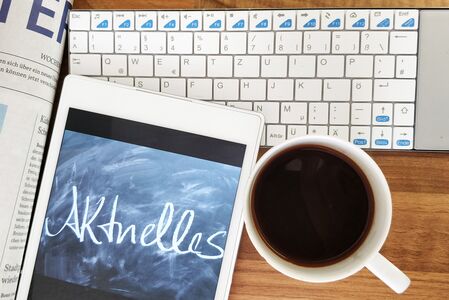 Das Symbolbild für aktuelles zeigt auf einem Tisch eine Zeitung, ein Tablet, eine Tastatur und eine Tasse Kaffee von oben. Alle Gegenstände sind weiß, auf dem Tablet steht "Aktuelles".