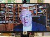 Ein Bildschirm, auf dem der Erzbischof zu sehen ist. Er sitzt in einer Bibliothek und liest seine Rede in die Kamera.