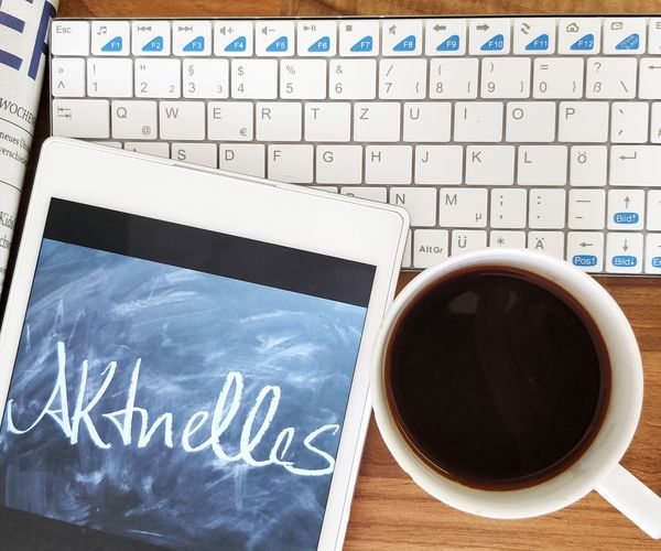 Das Symbolbild für aktuelles zeigt auf einem Tisch eine Zeitung, ein Tablet, eine Tastatur und eine Tasse Kaffee von oben. Alle Gegenstände sind weiß, auf dem Tablet steht "Aktuelles".